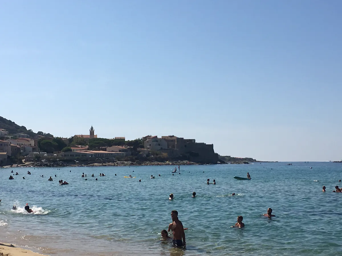 Badende am Strand von Algajola mit dem Küstenort im Hintergrund